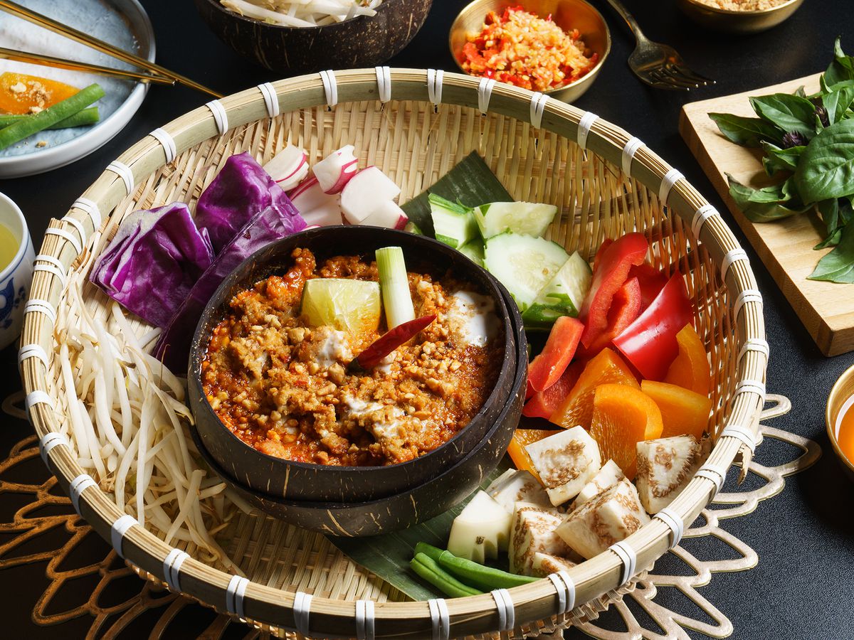 A basket holds an array of chopped vegetables and a small dark bowl with a rich stewy dish inside.