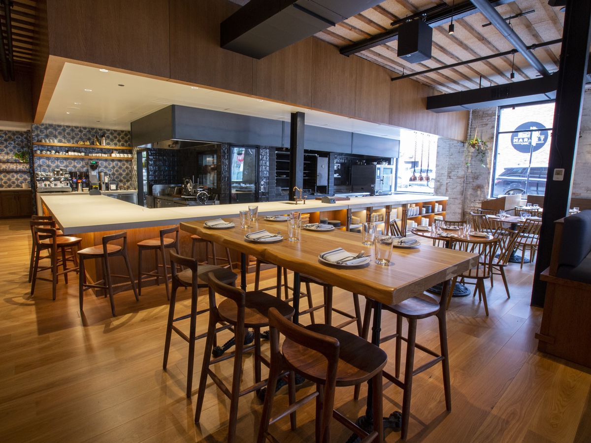 A bright dining room in a restaurant with black and white tile, light wooden floors, and bar stools with full backrests.