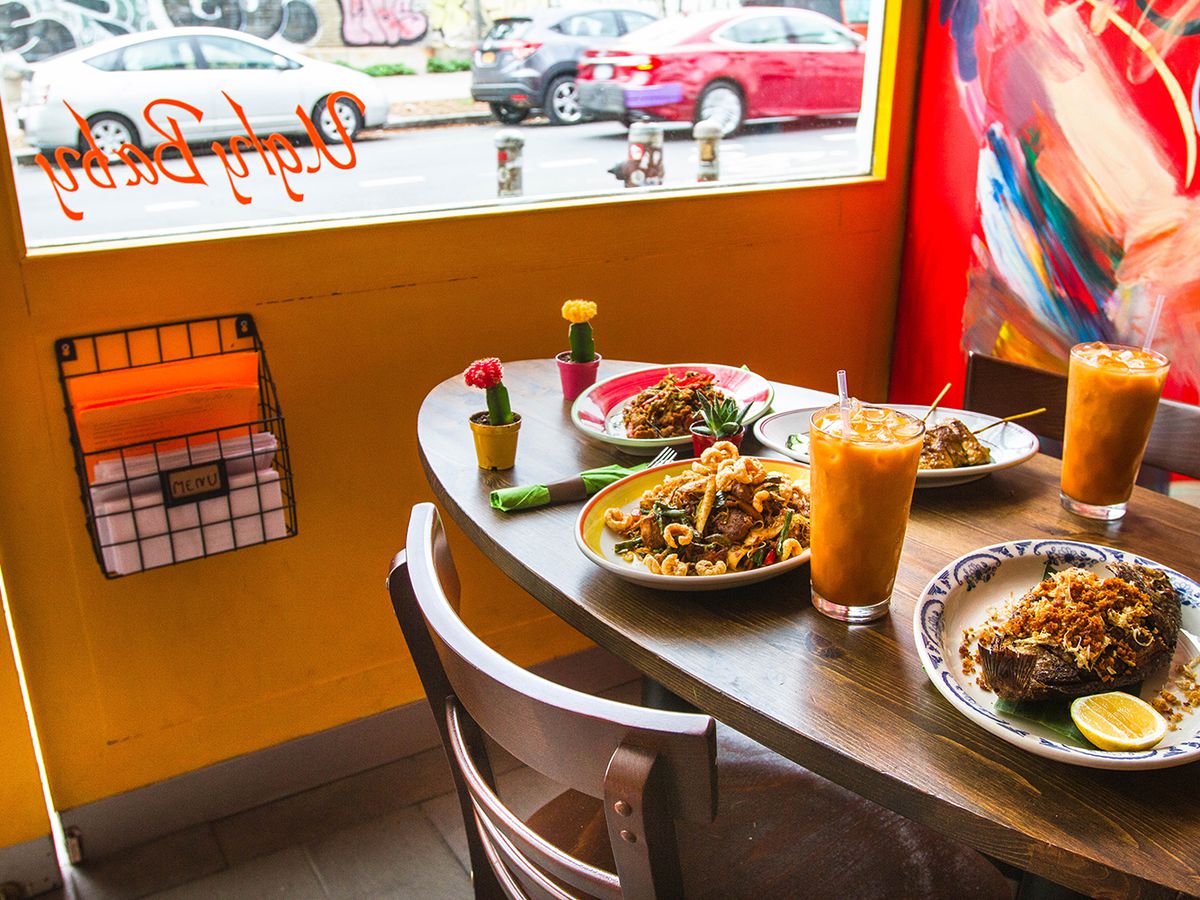 A dining room table with several dishes, two orange beverages with ice cubes, and a few ornamental, palm-sized cacti.
