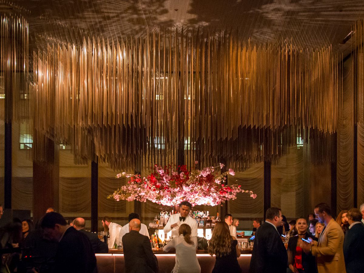 A man in a white tuxedo stands behind the bar at the Grill, in front of a giant arrangement of pink and red flowers