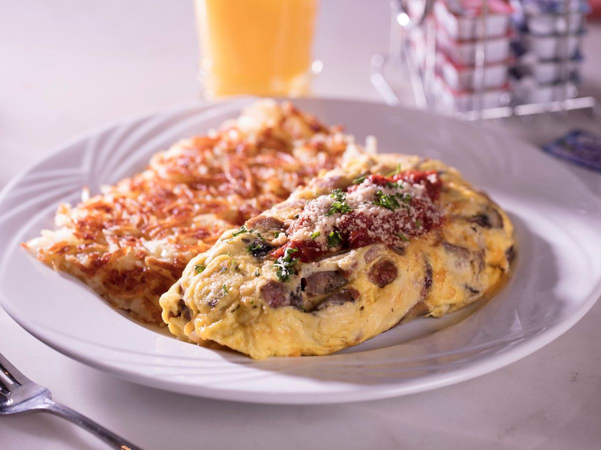 An omelet next to hash browns, on a white plate, next to orange juice.