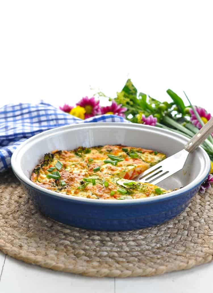 Mixed vegetable pie in a blue pie plate sitting with a slice taken out