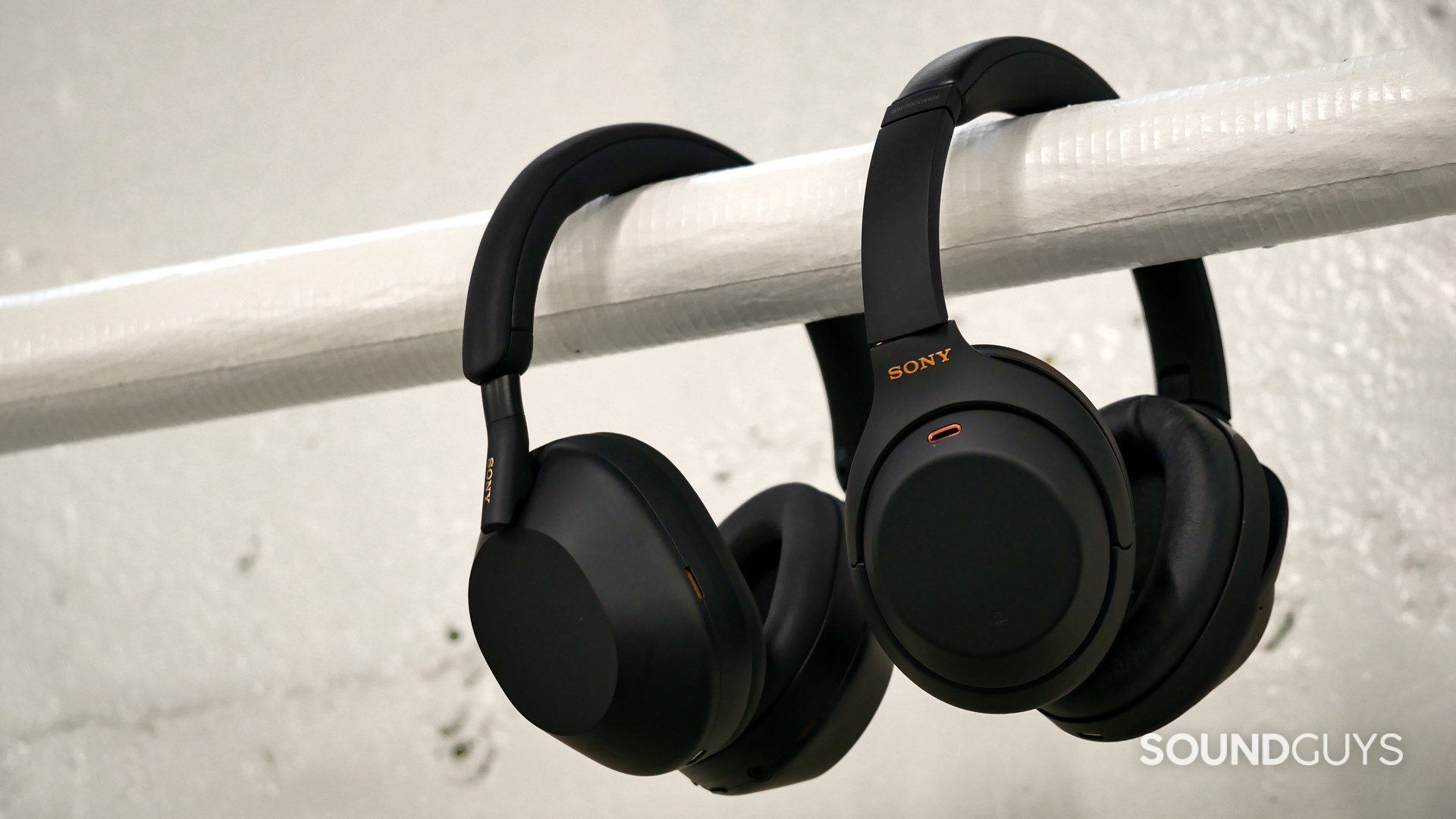 Side-by-side comparison of the Sony WH-1000XM5 (left) and the Sony WH-1000XM4 (right) hanging over a white horizontal pipe