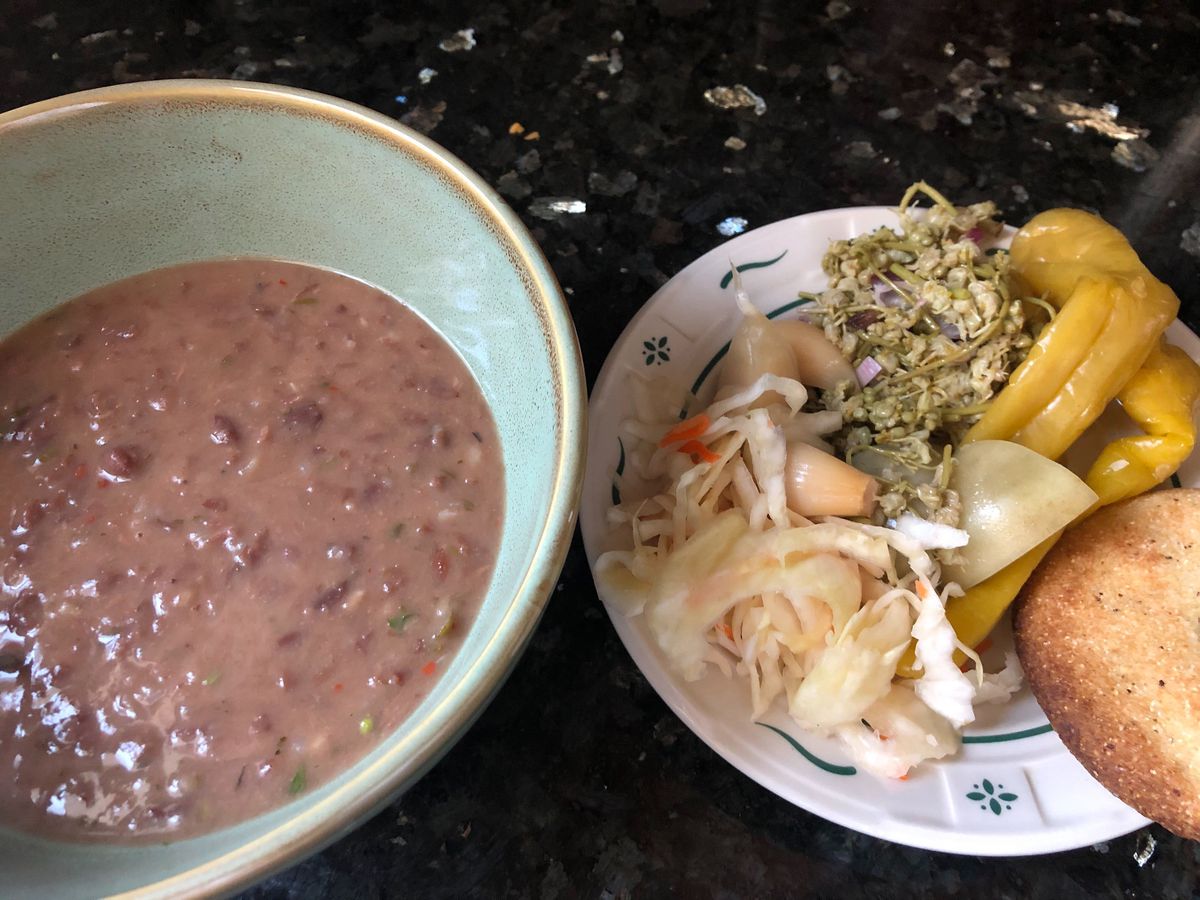 The image presents a teal bowl filled with red bean stew alongside a white plate adorned with an assortment of fermented vegetables.