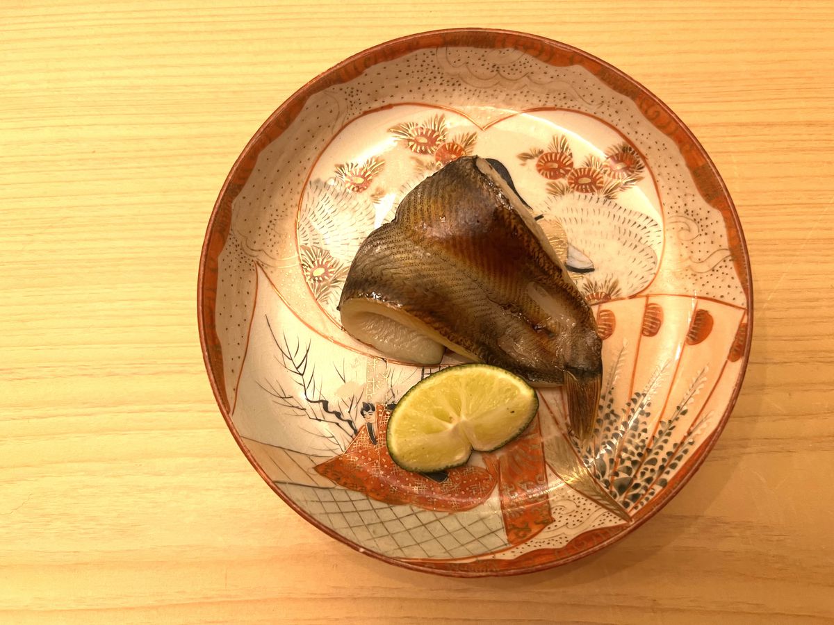 The image showcases a curled fish filet on a decorative plate, with a lime wedge placed beside it.