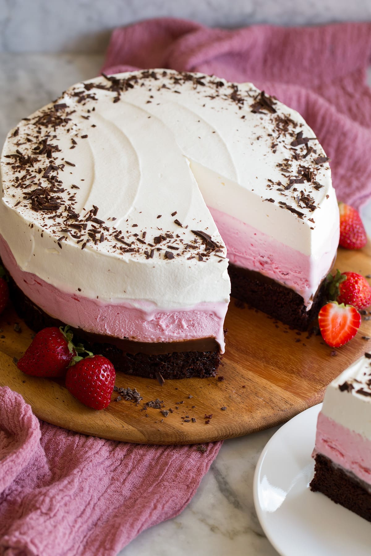 Whole ice cream cake with one slice removed. Layered with chocolate, strawberry, and vanilla.
