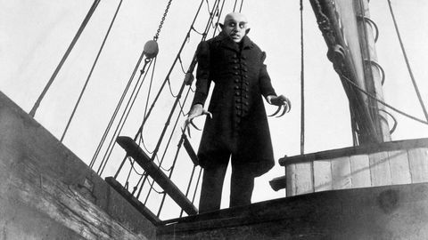 a vampirelike creature stands on the deck of a ship in a scene from nosferatu, a good housekeeping pick for best halloween movies
