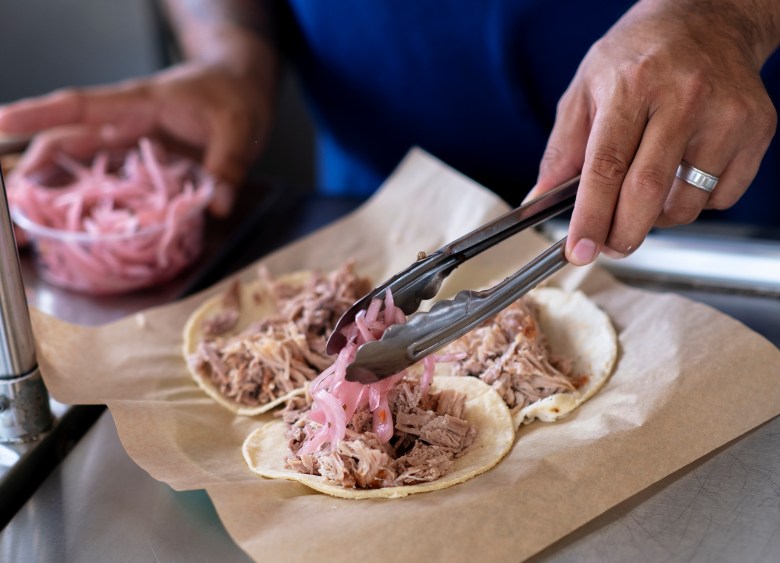 Carnitas Lonja chef Alex Paredes adds pickled onions to a carnitas taco on Wednesday.